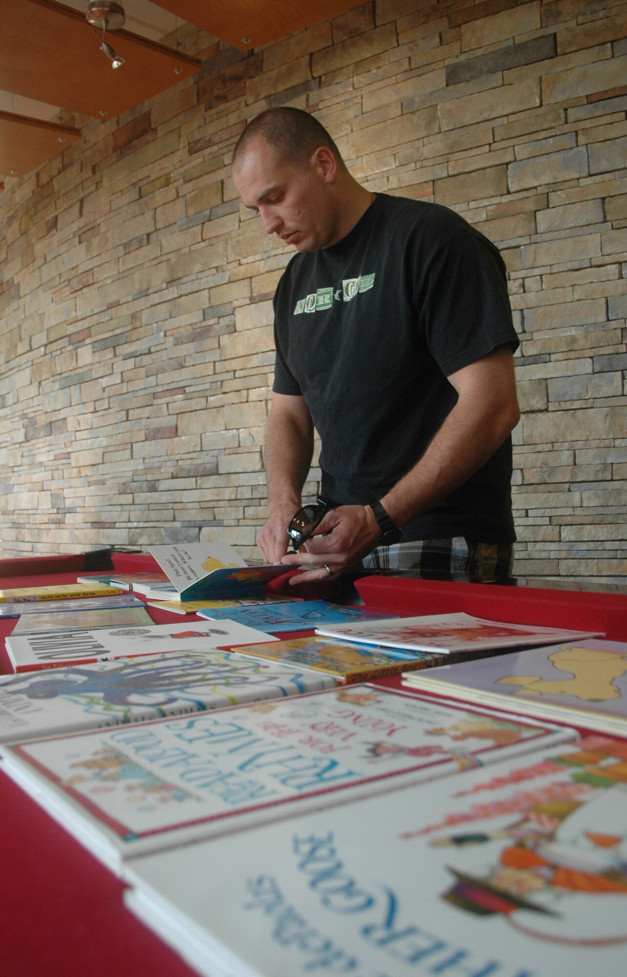 Tech. Sgt. David Aceveda, a member of the 744th Communications Squadron, Joint Base Andrews Naval Air Facility, Md., and spouse of Master Sgt. Veronica Aceveda, 512th Airlift Wing, Dover Air Force Base, Del., sifts through his options of books to read onto video Sept. 24 as part of the United Through Reading program inside the USO Community Center on Dover AFB. Deploying servicemembers can pre-record a DVD inside the USO's reading room, and the book and DVD will be sent to their child for free. (U.S. Air Force photo by Tech. Sgt. Scott Farley/Released)