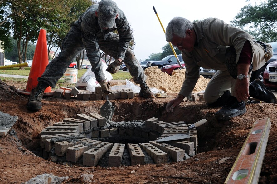 Airman 1st Class Rickey George, 2nd Civil Engineer Squadron, structural engineer, and Glynn Stephens masonry specialist, raise a manhole to eliminate groundwater from running into it at Barksdale Air Force Base, La., Nov 9. The 2 CES combines the talent of nearly 400 military and civilian members, who build, operate, maintain and protect $2.8 billion in real property. (U.S. Air Force photo/Senior Airman Brittany Y. Bateman)(RELEASED)