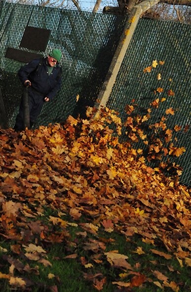 RAF MILDENHALL, England -- Barry Page, a base contractor, uses a leaf blower to move piles of leaves around Building 670 Nov. 10, 2010. Now that fall is giving way to winter, leaves are dropping from the trees and mounting up. Contractors load them onto a trailer, so they can be taken off base for recycling into mulch, which will eventually be added to top soil. (U.S. Air Force photo/Karen Abeyasekere)