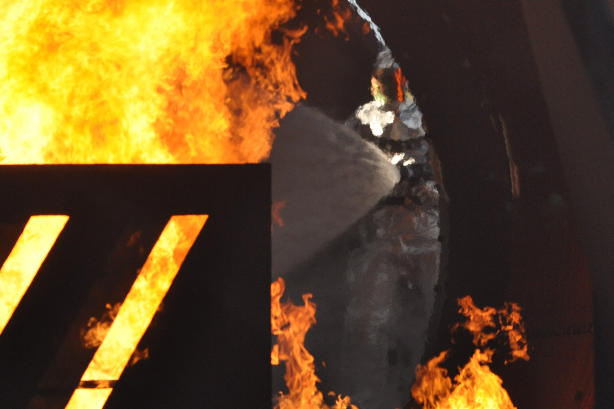 A safety officer with the 917th Civil Engineer Squadron oversees the entry of a team of firefighters into a burning wall of propane flames in a large frame aircraft trainer at Barksdale Air Force Base, La., Nov. 5, 2010. Approximately 20 members of the 917 CES were involved in this phase of the annual wartime training, which included extinguishing fires on both the outside and inside of the trainer. This particular team was lead by Col. John J. Mooney, commander, 917th Wing. Colonel Mooney decided to take up the challenge, in order to experience and get a feel for what Airmen in his command go through on a daily basis. For the professional firefighters, it is a part of their annual Air Force Certification process for Airport Rescue Firefighting. (U.S. Air Force photo/Tech. Sgt. Jeff Walston) 

