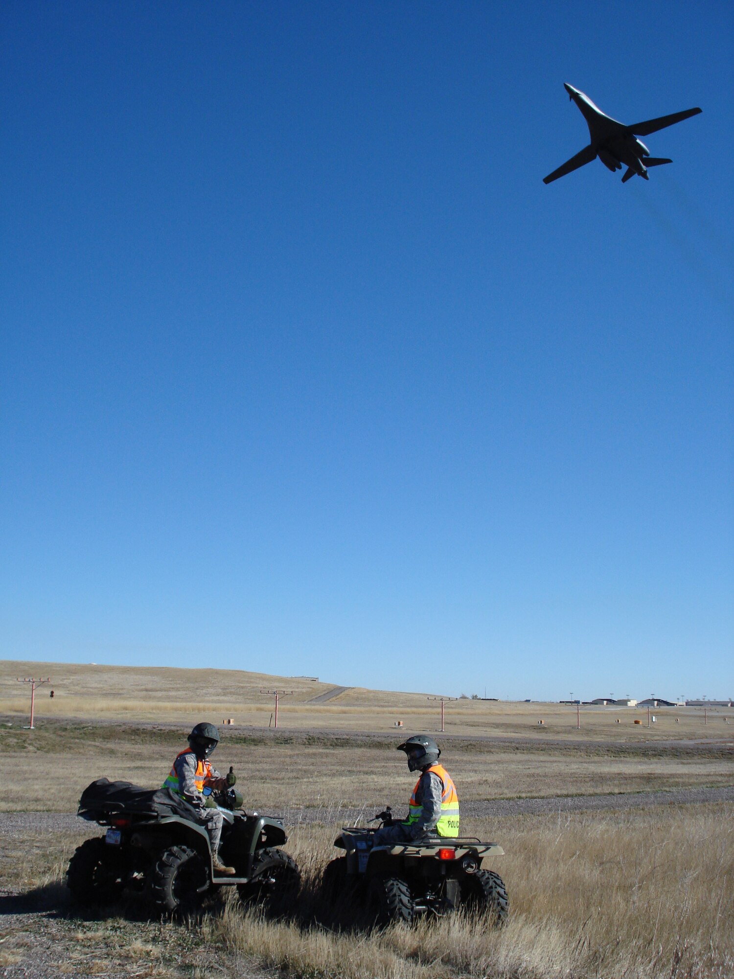 ELLSWORTH AIR FORCE BASE, S.D. - A B-1B Lancer flies above Col. Trent Edwards, 28th Mission Support Group commander and Col. Jeffrey Taliaferro, 28th Bomb Wing commander while they perform a perimeter check with 28th Security Forces Squadron Airmen. The SFS Airmen perform the checks regularly to ensure the integrity of the base perimeter. (Courtesy photo/Master Sgt. Carlos Moore)