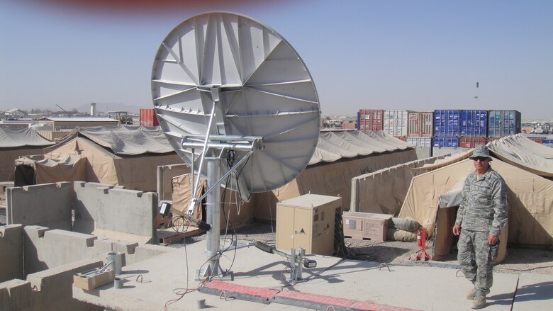 Deployed civilian Kamal “Kam” Pourrahman, of the 38th Cyberspace Engineering Group, walks by a morale net Wi-Fi satellite dish. The apparatus allows air expeditionary wing personnel at Kandahar Air Field, Afghanistan, to connect with family back home. (Courtesy photo)