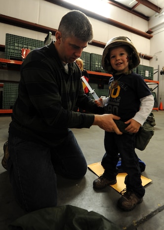 Maj. Jason Campbell equips his son Andrew, 3, with a web belt and canteen during the Children's Deployment Line Nov. 13, 2010, on Joint Base Charleston, S.C. The Children's Deployment Line consisted of face painting, briefings, picking up combat gear, touring a C-17 and finally eating simulated Meals, Ready-to-Eat (MREs) for lunch. Major Campbell is the 628th Civil Engineer Squadron, Operations Flight commander. (U.S. Air Force photo/Senior Airman Timothy Taylor)