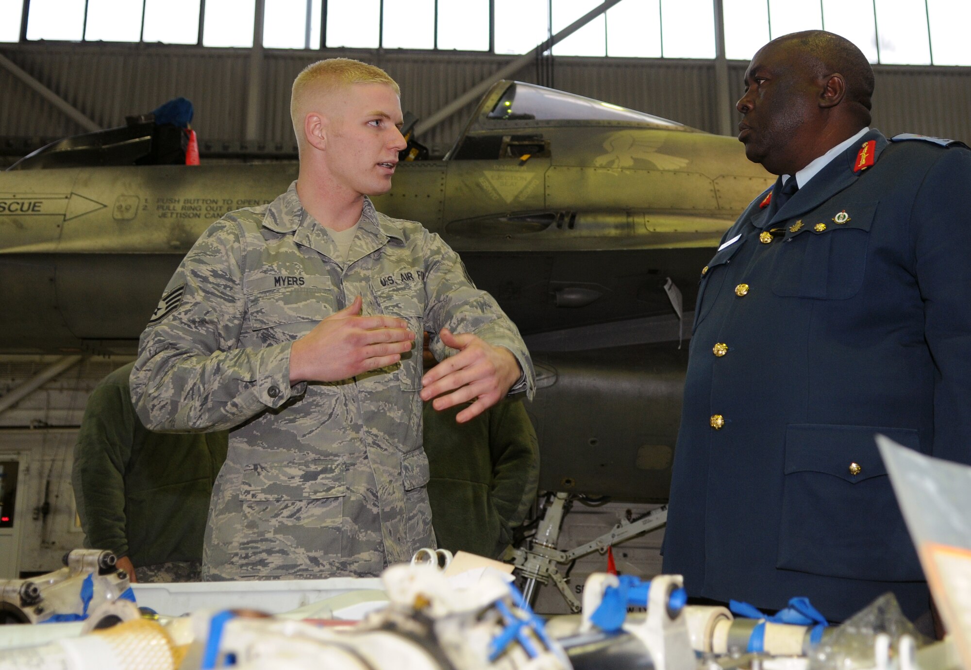 SPANGDAHLEM AIR BASE, Germany – Staff Sgt. Greggory Myers, left, 52nd Equipment Maintenance Squadron F-16 Fighting Falcon phase floor chief, explains to Maj. Gen. Jim Beesigye Owoyesigire, Ugandan Peoples Defense Air Force commander, how the use of a loading trailer can cut the maintenance time of an F-16 in half Nov. 11. General Owoyesigire toured several squadrons on Spangdahlem Air Base during his visit to gain a greater understanding of how the U.S. Air Force operates. (U.S. Air Force photo/Staff Sgt. Benjamin Wilson)