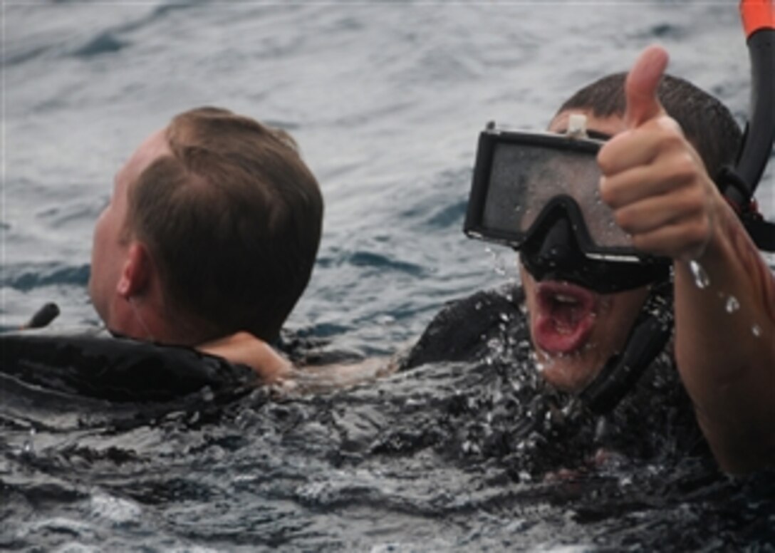 U.S. Navy Petty Officer 3rd Class Andres Acosta (right) signals to a boat crew while rescuing Petty Officer 1st Class Kurt Bartholomai during search and rescue swimmer training in the Java Sea on Nov. 8, 2010.  Acosta is assigned to the amphibious assault ship USS Essex (LHD 2), which is part of the permanently forward-deployed Essex Amphibious Ready Group on patrol in the Western Pacific Ocean.  