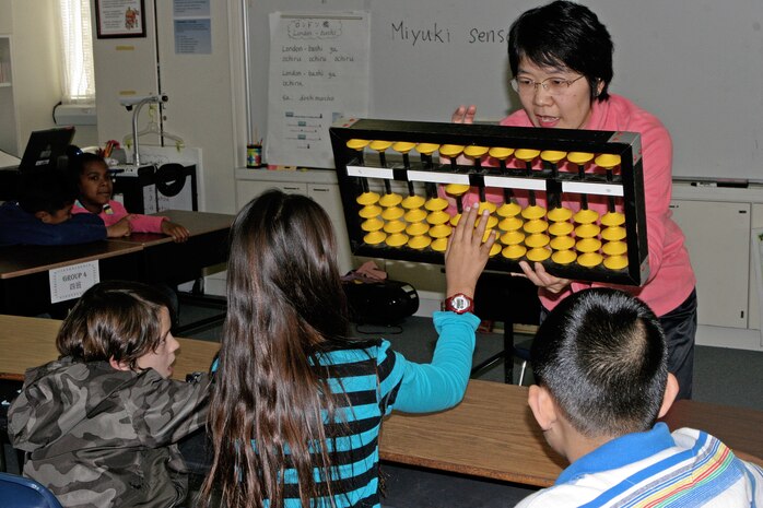 Miyuki Inoashi, a master teacher of soroban, makes sure students understand how to use the tool by having them demonstrate on her much larger version during a training session at Matthew C. Perry Elementary School here Nov. 16. Soroban is an advanced mathematical ability supporting one’s mental calculation aptitude and facilitates a better understanding of the number concept, base ten systems and place value.
