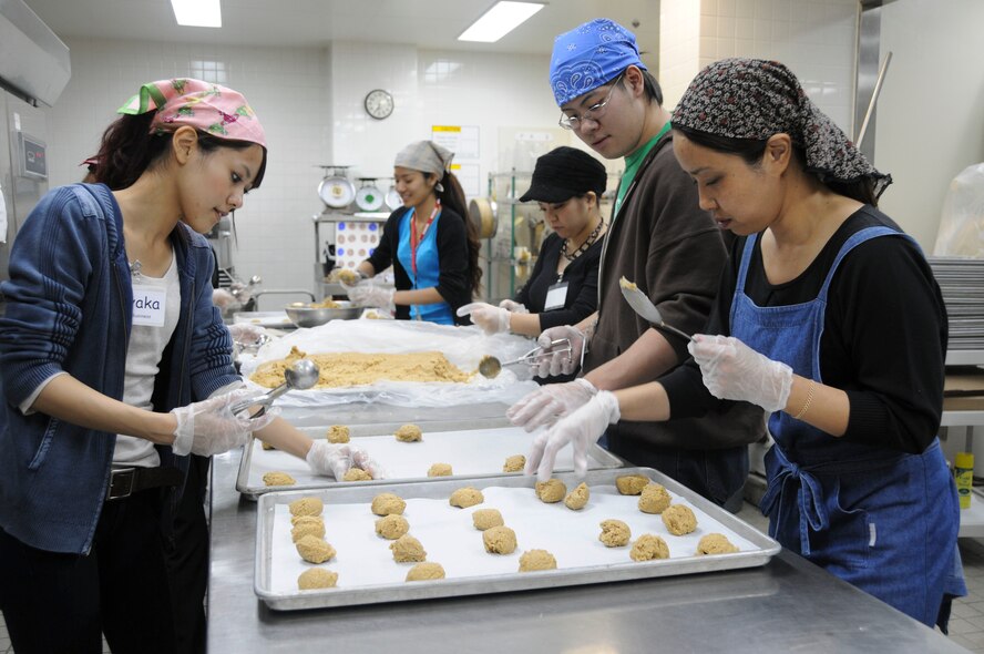 Ms. Sayak Higa, Mr. Yoshinori Kitagawa, and Ms. Makako Miyara place cookie dough onto trays before they are placed in the oven at Kadena Air Base Nov. 16. The local community assisted in making 2,500 packages of cookies for all military dorm residents. (U.S. Air Force photo/Staff Sgt. Darnell T. Cannady)