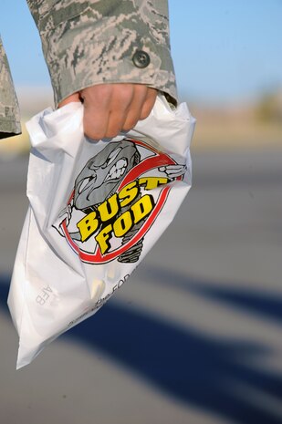 NELLIS AIR FORCE BASE, Nev. -- An Airman carries a "Bust FOD" bag during a Foreign Object Debris walk Nov. 15. The bags were used to throw any FOD or trash away during the FOD walk. FOD prevention is every individual's responsibilities as it can cost millions of dollars of damage to aircraft systems and personnel. (U.S. Air Force photo by Senior Airman Brett Clashman)(Released)