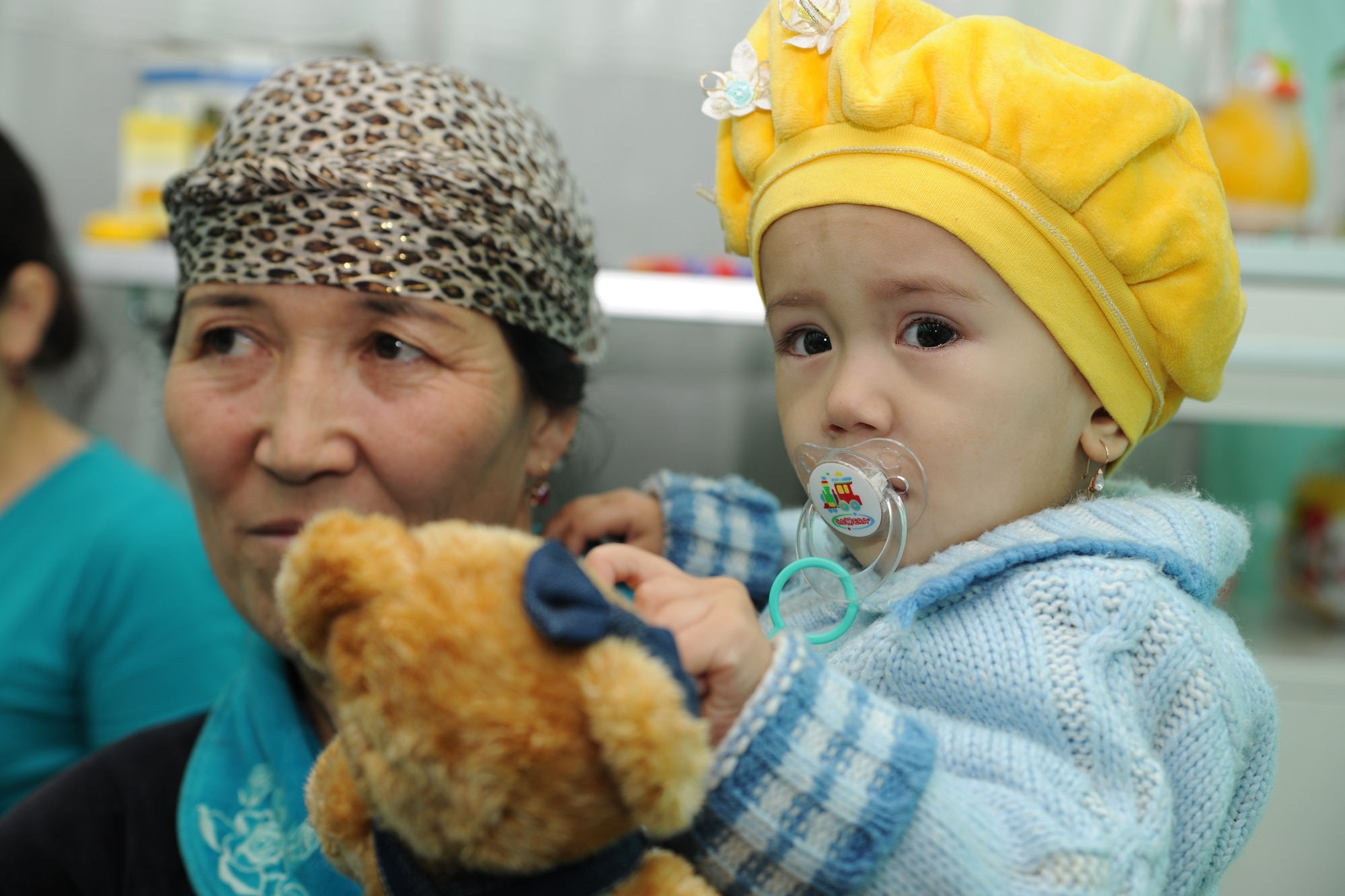 BISHKEK, Kyrgyzstan -  A child, patient at the Children's Cancer Center in Bishkek, is held in her mother's arms while she plays with her new bear received from members of the Transit Center at Manas Nov. 13.  Members from the Transit Center at Manas visited the children as part of a team to assess the needs of the facility.  (U.S. Air Force photo/Staff Sgt. Nathan Bevier)
