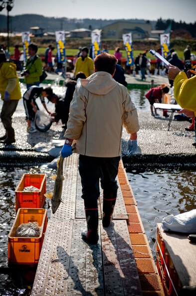 A Japanese man walks along a metal boardwalk carrying his freshly caught salmon during the Oirase Salmon Catching Festival at Salmon Park, Oirase, Japan, Nov. 13, 2010. After exiting the wading pool, participants were treated to hot salmon stew to combat the cold weather and wet clothing. (U.S. Air Force photo by Staff Sgt. Samuel Morse/Released)