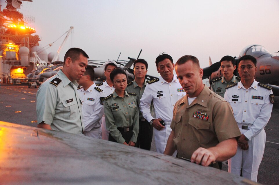 Lt. Col. Joshua Luck, commanding officer, Marine Attack Squadron 542, 31st Marine Expeditionary Unit, briefs visiting Chinese Senior Capt. Xujing Cai, Navy chief of staff, Hong Kong Garrison, People’s Liberation Army (center, in white) and other visiting Chinese military officers on AV-8B Harrier jet aircraft capabilities during a flight deck reception aboard the USS Essex (LHD 2) in Hong Kong harbor, Nov. 17.