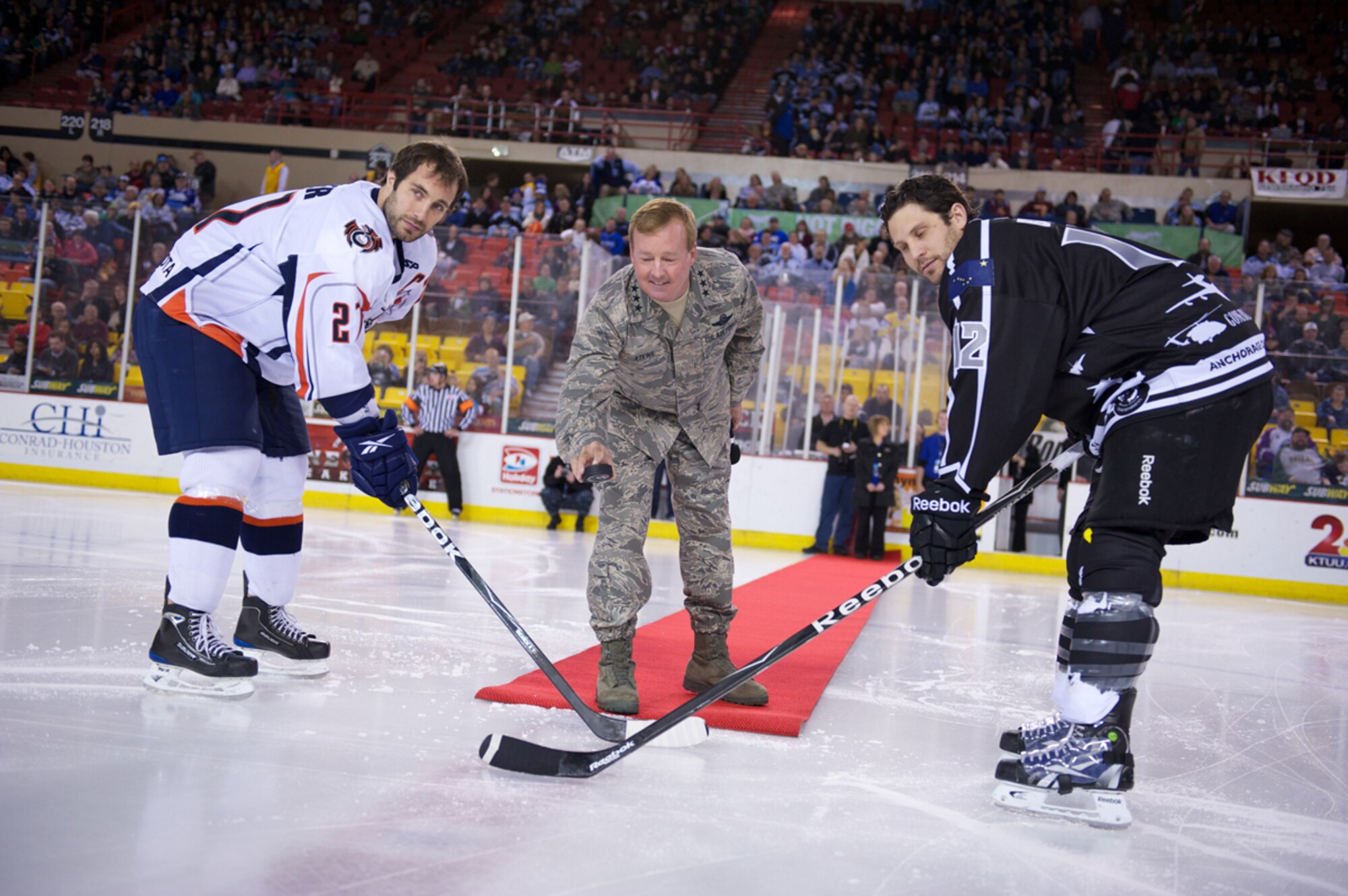 Air Force Lt. Gen. Dana Atkins, commander, Alaskan Command, drops a ceremonial puck between Ontario Reign No. 27 David Walker and Alaska Aces No. 12 Scott Burt, before an Aces military appreciation game. (Photo by David Bedard/JBER PAO) 