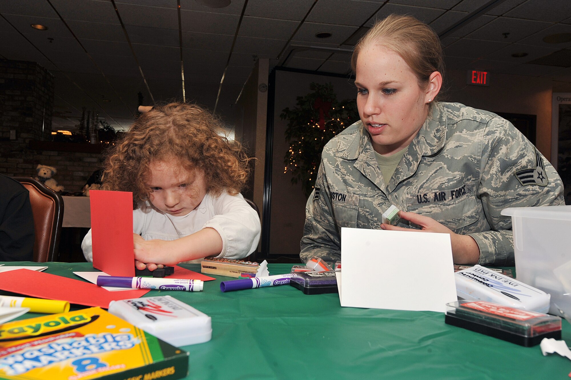 OFFUTT AIR FORCE BASE, Neb. -- Alessandra Wright, daughter of Lt. Col. Kurtis Wright, makes a card for her father while Senior Airman Jennifer Houston, a volunteer from the 55th Aerospace Medical Squadron, assist sher during the holiday connections event in the Community Center here Nov. 16. More than 100 Team Offutt families attended and made gifts, cards and video messages for their loved ones who will be away from home this holiday season. The annual event, established in 2000, provides a fun environment  for families to come together and share a little joy. U.S. Air Force photo by Charles Haymond