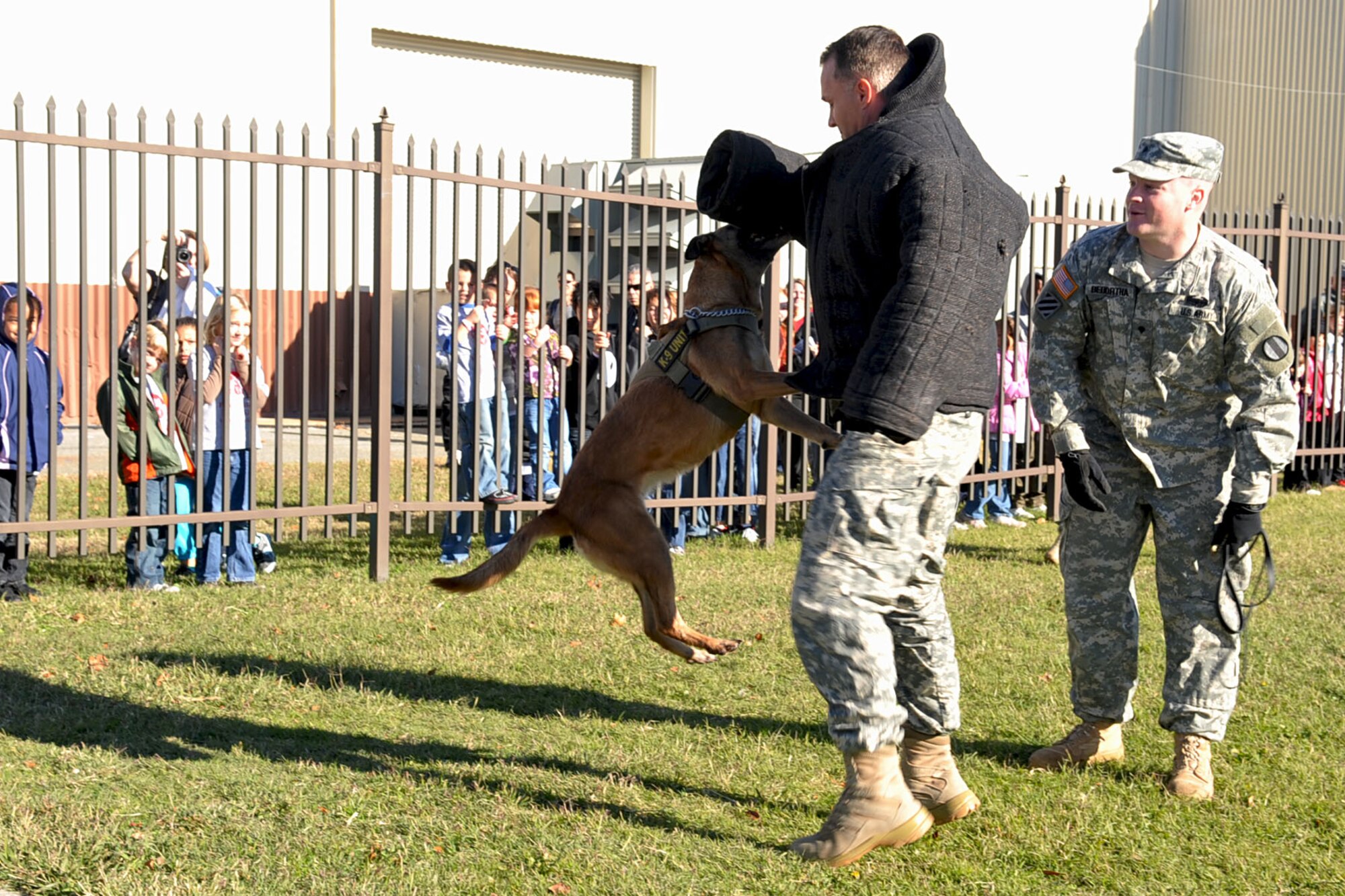 LANGLEY AIR FORCE BASE, Va. -- Sgt. Mathew Stoner, Fort Eustis 221st Military Police Detachment, and Chay, Military Working Dog, demonstrate the abilities of a trained MWD while Spc. Matthew Bedortha explains their actions during the Operation Hero event at the static display hanger Nov. 13. The annual event is held to give military children the experience of what their parents go through during the pre-deployment process. (U.S. Air Force photo/Staff Sgt. Ashley Hawkins)(RELEASED)