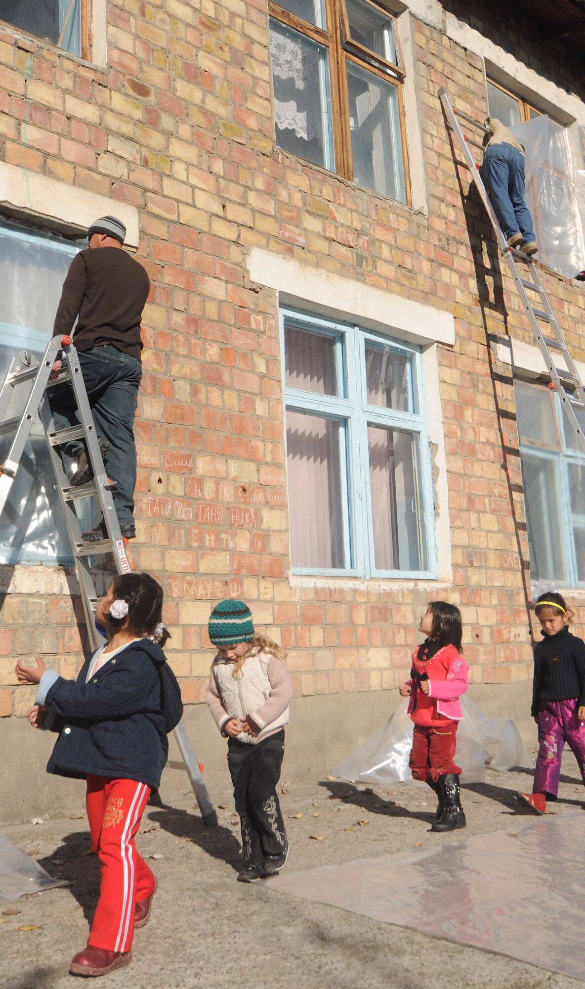 VASILIEVSKOE VILLAGE, Kyrgyzstan -  Staff Sgt. James Procaccini (left), 376th Expeditionary Civil Engineer Squadron humanitarian assistance, and Tech Sgt. Ron Warlick, 376th Expeditionary Communications Squadron, staple plastic over 20-year-old windows at Vasilievskoe Kindergarten as children return to class from a break Nov. 17.  The plastic will create a vapor barrier allowing most of the warm air to stay in the facility during Winter.  Over $10,000 have been spent on renovations for the school to include new windows and doors.  (U.S. Air Force photo/Staff Sgt. Nathan Bevier)
