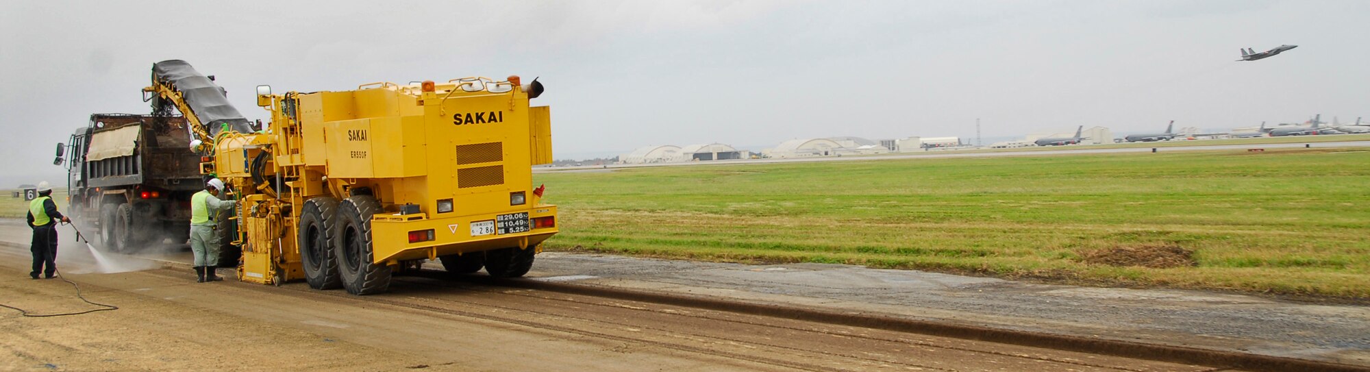 A Kadena F-15 takes off from Kadena's northern runway while local contractors renovate the southern runway Nov. 16. As the reconstruction continues, the contractors take measures like wetting down the milled asphalt to keep debris down as it's transferred into a dump truck to be recycled and used in future Okinawan road projects. (U.S. Air Force photo/ Airman 1st Class Maeson L. Elleman)