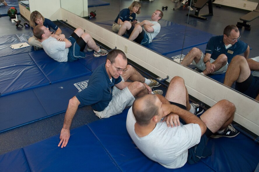HANSCOM AIR FORCE BASE, Mass. – Fitness Testing Technicians Barbara Cook (left) and Stephen Grant administer the sit up portion of the fitness assessment with Airman 1st Class Steve Anderson (second from left) and Capt. Nicomedez Correa on Nov. 16. New winter fitness assessment procedures took effect this month. (U.S. Air Force photo by Rick Berry)