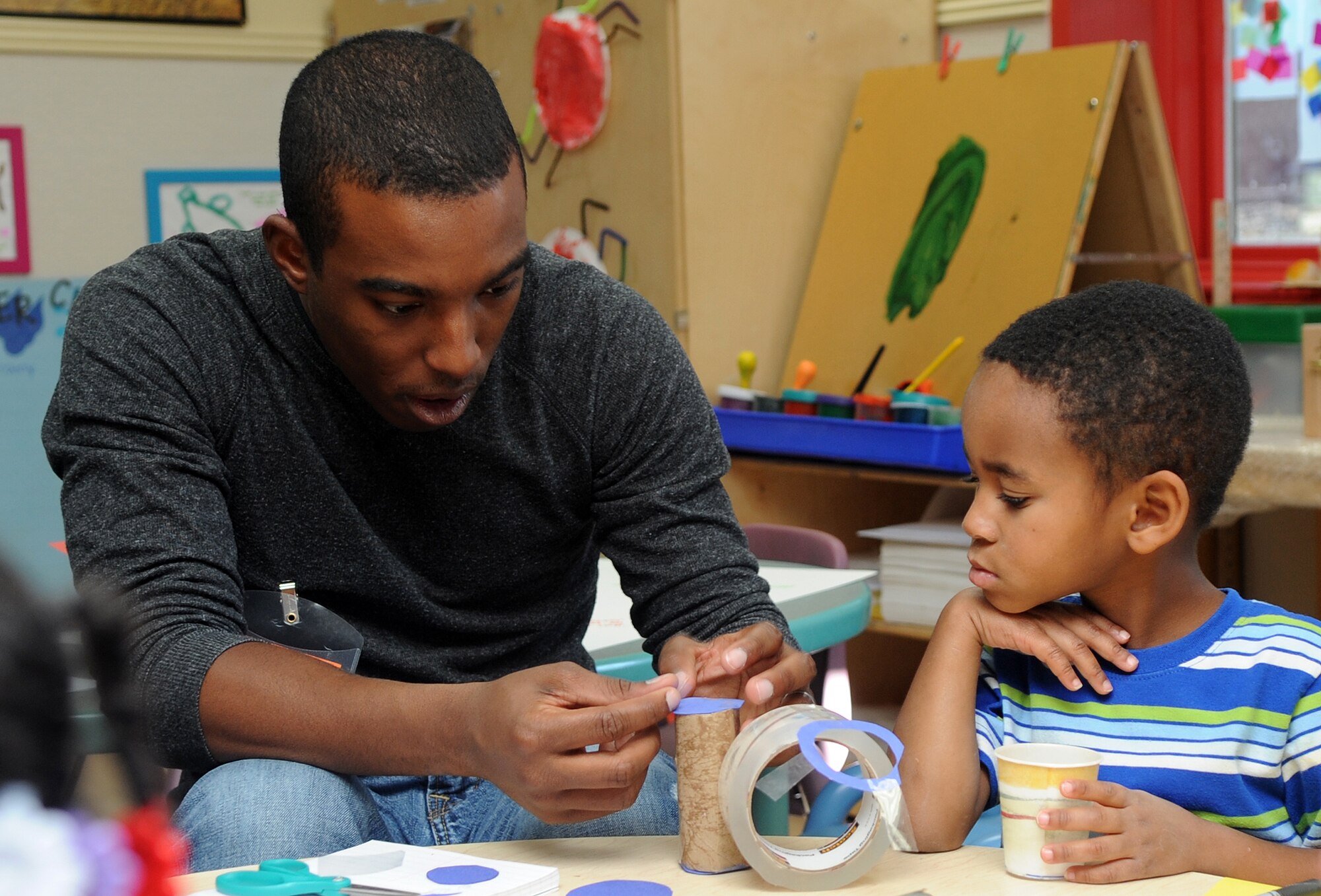 Buckley Air Force Base, Colo.- Airman 1st Class Paul Labbe helps a class make rain sticks for Native American Heritage month at the Child Development Center where volunteers from the Team Buckley spent the afternoon finger painting and making rain sticks. ( U.S. Air Force Photo by Airman First Class Marcy Glass )