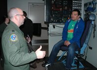 JOINT BASE LEWIS-MCCHORD, Wash.- Comedian Carlos Mencia, sits in a loadmaster seat of a C-17 Globemaster III simulator as Capt. Eric Hodges, a pilot and Reservist with the 728th Airlift Squadron, explains the capabilities of the C-17, Nov. 19. Experiencing the simulator was part of Mencia's "Tour for the Troops", sponsored by the Air Force Reserve. Mencia gave a stand-up performance at McChord Field that evening for almost 2,300 troops from all branches of the military. (U.S. Air Force photo/Master Sgt. Jake Chappelle)