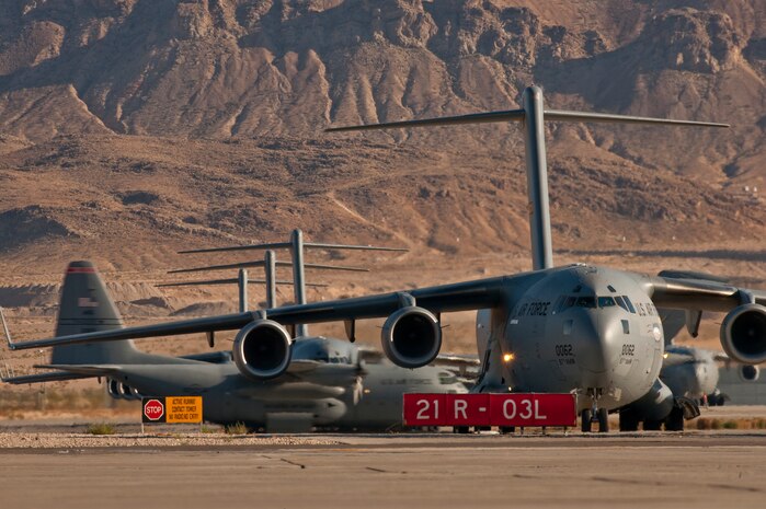 NELLIS AIR FORCE BASE, Nev. --  C-17 Globemaster III aircraft Line up on the Nellis taxiway as  a C-130 Hercules lands during the Mobility Air Forces Exercise held at Nellis and over the Nevada Test and Training Range,  Nov 17. Approximately 40 C-17 Globemaster III and C-130 Hercules cargo aircraft will assemble in aerial formations over the NTTR to conduct air and ground operations as part of the bi-annual, U.S. Air Force Weapons School Mobility Air Forces Exercise.  (U.S. Air Force photo by Tech. Sgt. Michael R. Holzworth)(Released)