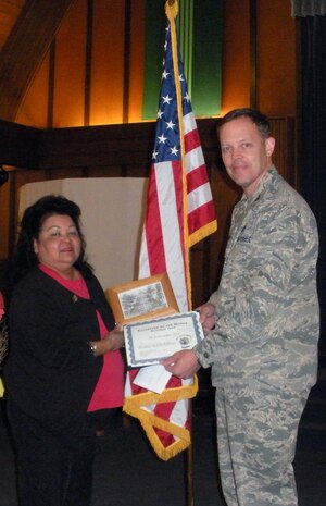 NELLIS AIR FORCE BASE, Nev.-- Col. Steven Garland, 99th Air Base Wing commander, presents Kini Miller-Gore a coin and certificate of appreciation Nov. 17 at the Base Chapel. Mrs. Miller-Gore was named the October Volunteer of the Month for Nellis. The Airman and Family Readiness Center hosts the volunteer program for the base, and anyone interested in volunteering in the local community should call the center at 652-3327. (Courtesy photo)