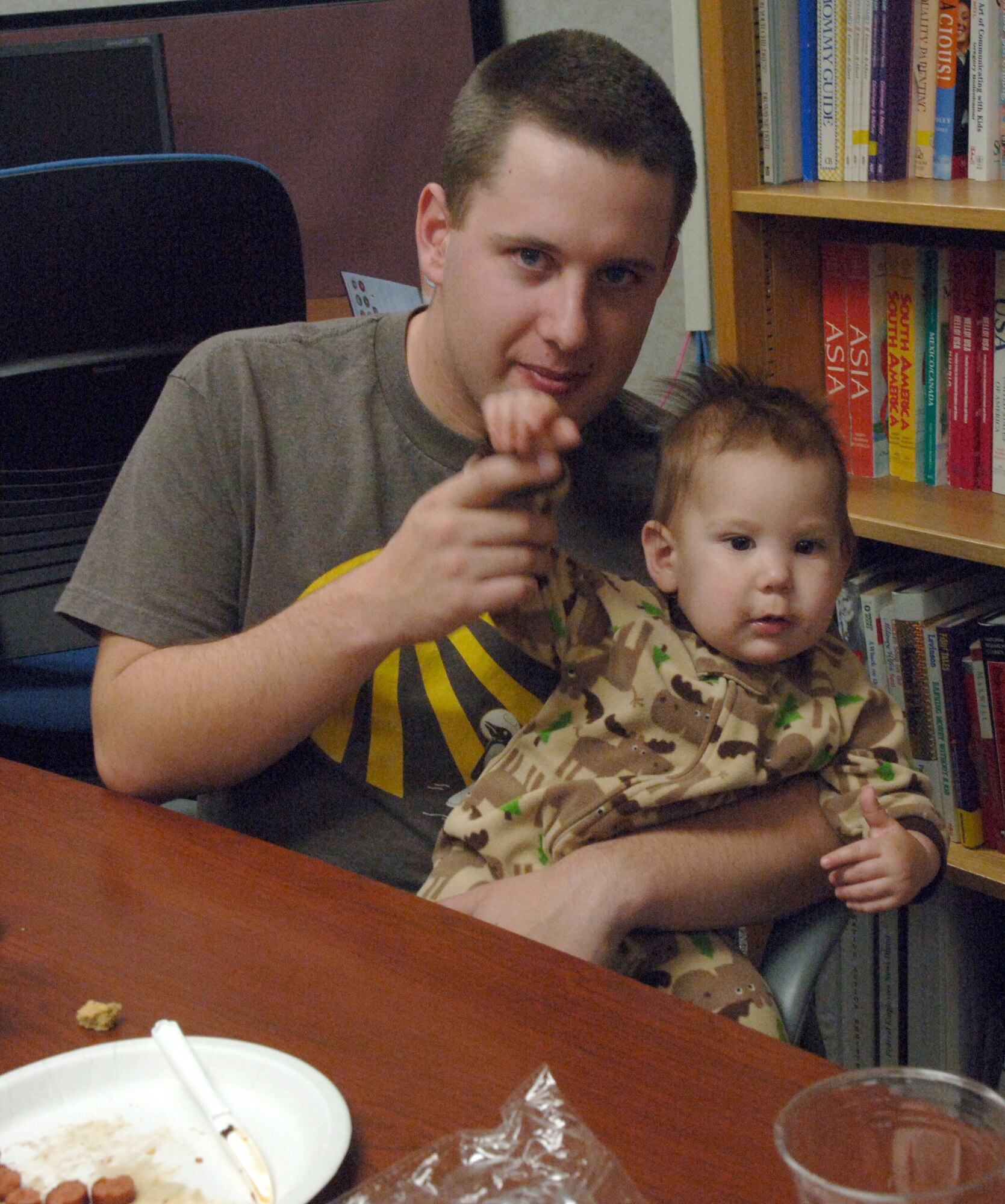 Airman 1st Class Mark Rady, 319th Civil Engineer Squadron, waves his son’s hand after feeding him dinner during the 4th Annual Airman and Family Readiness Center Soup Supper, Nov. 23 at the A&FRC. The soup supper is one of the four quarterly open houses the A&FRC hosts to show off the services they provide to both single Airmen and to Airmen with families. The event included ten different homemade soups and stews, desserts, arts and crafts, and a holiday movie. (U.S. Air Force photo by Airman 1st Class Rachel Waller)