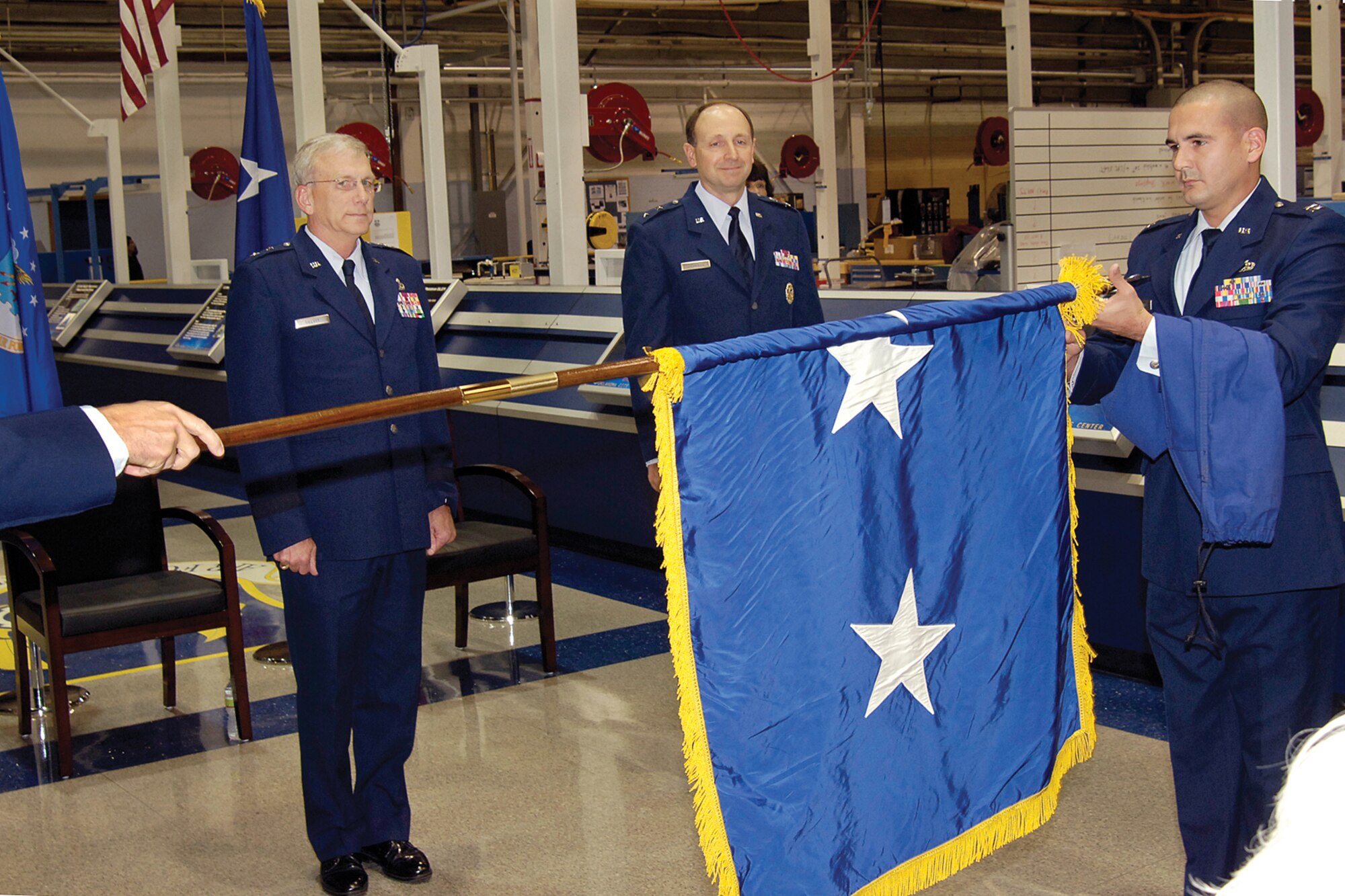 Moments after being promoted, Maj. Gen. Bruce Litchfield, right, watches as his two-star flag is unfurled by Capt. Jarod Castaneda. Oklahoma City Air Logistics Center Commander Maj. Gen. David Gillett presided over the Nov. 12 ceremony held at Hollywood and Vine in Bldg. 3001 for the commander of the 76th Maintenance Wing. (Air Force photo by Margo Wright)