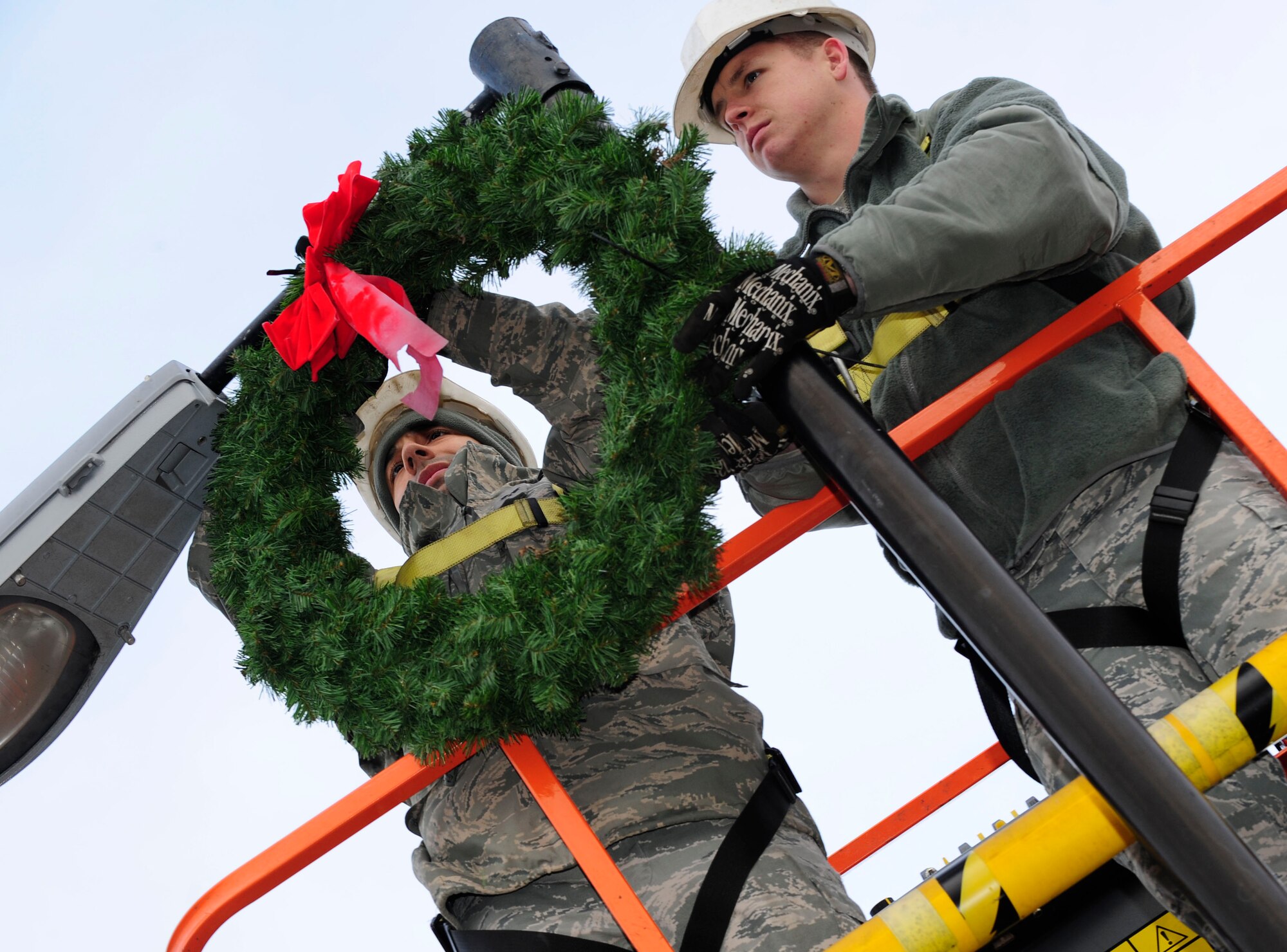 RAF MILDENHALL, England -- Senior Airman Roberto Rodriguez III, 100th Civil Engineer Squadron electrical journeyman, and Senior Airman Scott Ricketts, 100th CES structural journeyman, work together to hang wreaths on light poles throughout RAF Mildenhall Nov. 22, 2010. The wreaths, along with other holiday ornaments, were hung around the base in preparations for the holidays. (U.S. Air Force photo/Senior Airman Ethan Morgan)