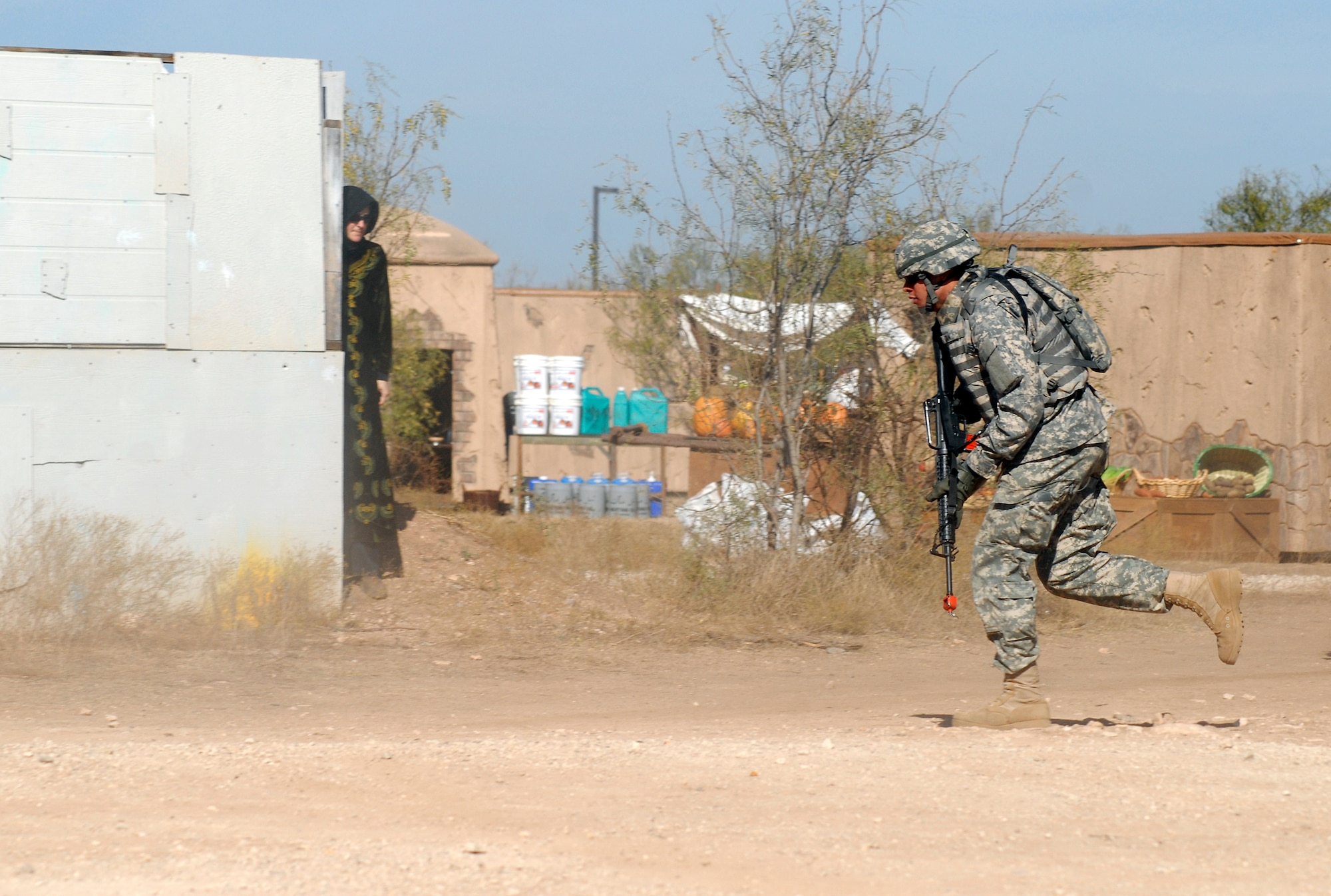 GOODFELLOW AIR FORCE BASE, Texas – A member of the 344th Military Intelligence Battalion runs to take up a new defensive position as a local Afghani role player looks on during a training scenario at a mock Afghanistan village.  The 344th MI BN took time to show visitors some of the possible situations they may encounter while deployed to Afghanistan during the annual Goodfellow Community Appreciation Day Nov. 20.  Goodfellow opened its doors for the day to allow the local community the opportunity to get a glimpse of the vital mission that the base performs.  (U.S. Air Force photo/Master Sgt. Randy Mallard)