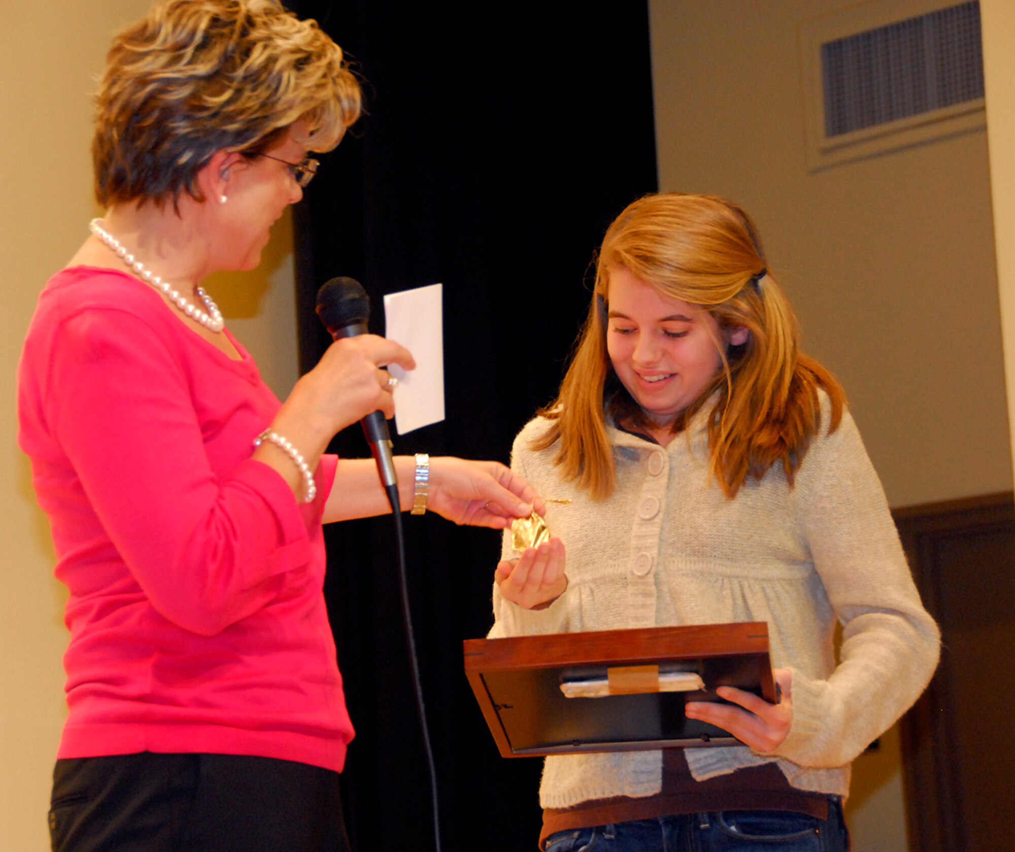 Carol Malackowski, wife of Col. Patrick Malackowski, 51st Fighter Wing commander, presents Maggie Dene, a ninth-grade student at Osan American High School, a wing coin and certificate of recognition from the American Red Cross for “Extraordinary Personal Action” during an awards ceremony at the school Nov. 22. (U.S. Air Force photo/Staff Sgt. Eunique Stevens)
