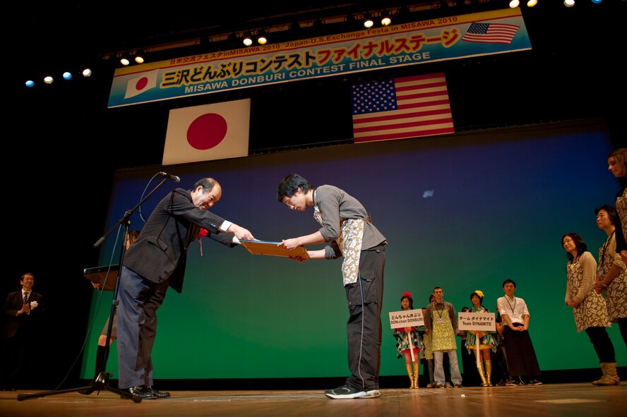 Yota Shimoda (right) accepts the Misawa Donburi Contest grand prize on behalf of his team, Team Hersheys, during the closing ceremony of the contest, Nov. 27, 2010 at the Misawa Civic Center, Misawa, Japan. Five international teams competed for the title of best donburi, a category of traditional Japanese cuisine where various meats and vegetables are served over rice in a bowl. (U.S. Air Force photo by Staff Sgt. Samuel Morse/Released)