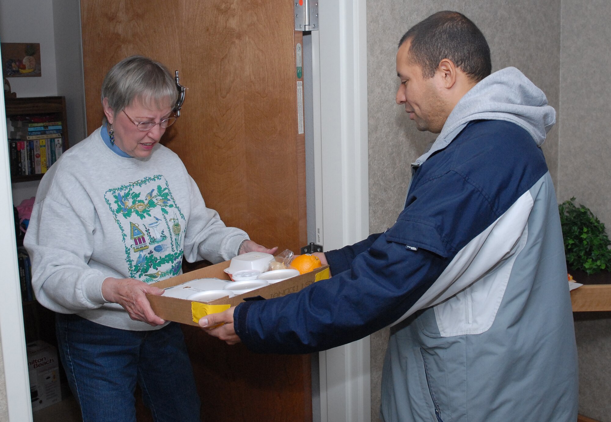 Senior Airman Rogerio Nascimento, 341st Force Support Squadron personnelist, hands Maxine Alebe a Thanksgiving meal Thanksgiving day. Airman Nascimento was among 47 volunteers who prepred and delivered 370 meals in the Great Falls area. (U.S. Air Force photo/Staff Sgt. Dillon White)