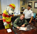 LAUGHLIN AIR FORCE BASE, Texas – Col. Michael Frankel, 47th Flying Training Wing commander, signs the declaration to recognize Oct. 3 through 9 as Fire Prevention Week at Laughlin as David Isbell, of Laughlin's Fire Department, and 'Sparky' look on. The Fire Department here will host several events including a search and rescue challenge. (U.S. Air Force photo by Airman 1st Class Blake Mize) 