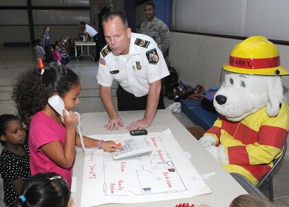 Gabrielle Dorsey, age 7, daughter of Esperanza Dorsey, learns how to call 911 during a house fire from Sparky the fire dog and Randolph Air Force Base fire chief Mark Ledford on Oct 5. The fire department holds a fire prevention event annually at the Randolph Elementary School.  
(U.S. Air Force photo/David Terry)
