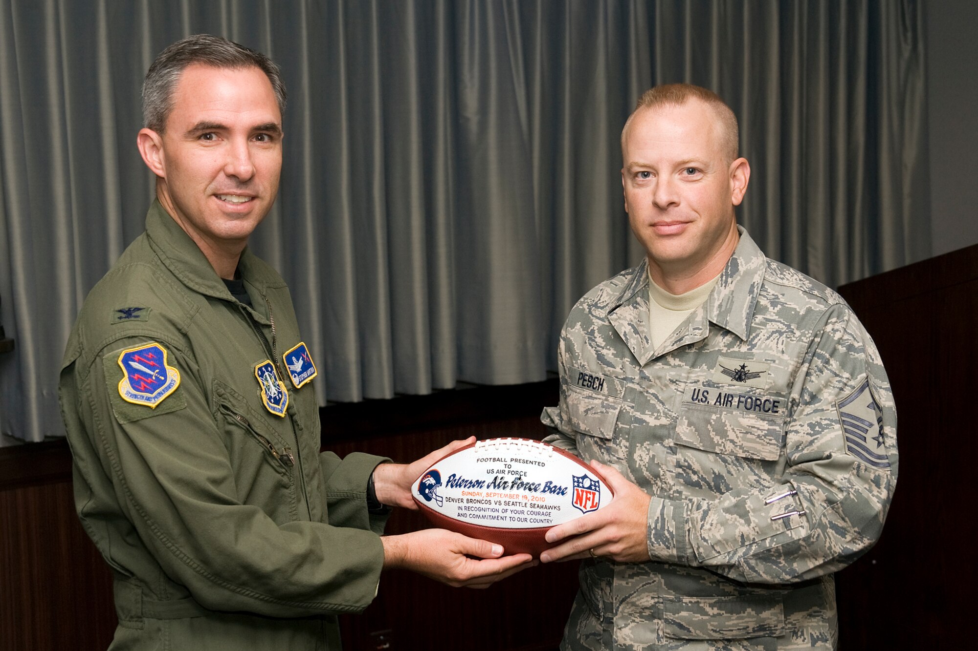 PETERSON AIR FORCE BASE, Colo. – Master Sgt. David Pesch, 21st Space Wing director of staff first sergeant, presents the Denver Broncos football game ball to Col. Stephen N. Whiting, 21st SW commander. The Broncos, who played the Seattle Seahawks at home, paid tribute to military members during their annual U.S. Military Appreciation Day pre-game ceremony Sept. 19. Members from the Air Force, Army, Navy and Marines were thanked for their service. Airmen, along with other military members, had the opportunity to meet former Denver Broncos quarterback and Hall of Famer John Elway and other Broncos players and each service branch received a souvenir game ball. The salute to the military has become a Broncos tradition. (U.S. Air Force photo/Larry Hulst) 