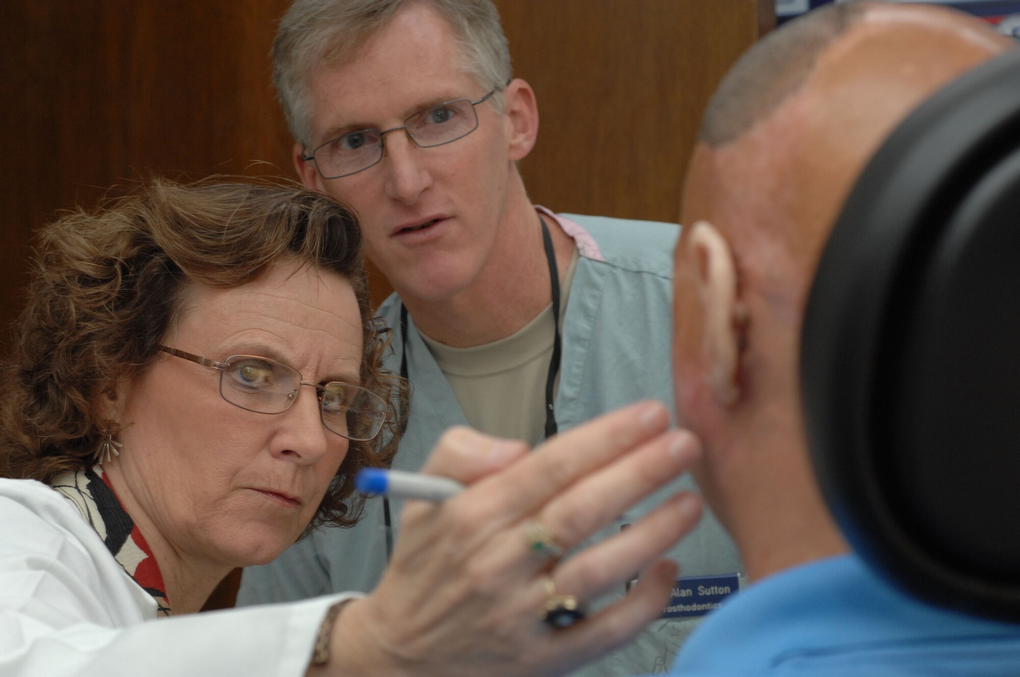 Ms. Nancy Hansen, accompanied by Col. (Dr.) Alan Sutton, director of the Maxillofacial Prosthetics Fellowship Program for the 59th Medical Wing, examines Army Staff Sgt. (Ret.) Shilo Harris, a wounded veteran, as he is fitted for prosthetic ears Oct. 5, 2010, at the MacKown Dental Clinic, Wilford Hall Medical Center, Lackland Air Force Base, Texas. As the only clinically certified anaplastologist in the Department of Defense, Ms. Hansen works closely with the fellowship program building prosthetics for wounded warriors. (U.S. Air Force photo /Staff Sgt. Robert Barnett) 

