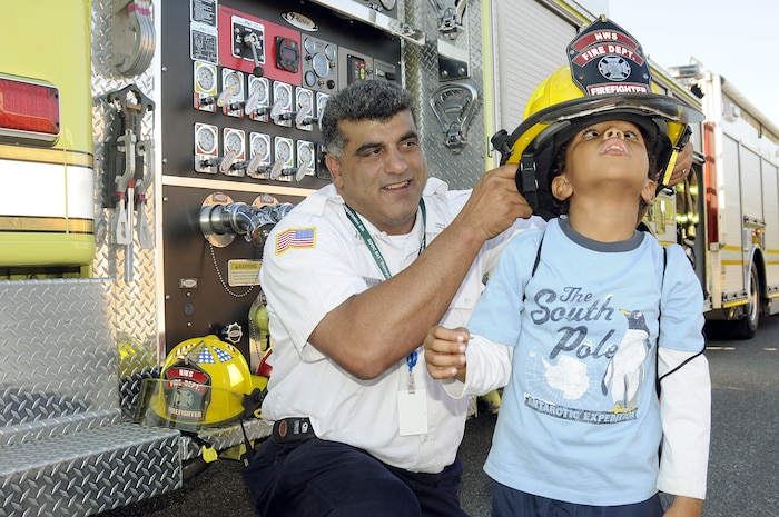 Captain Paul Wilkins (left), with the Joint Base Charleston-Weapons Station?s fire department, sets one of the fire helmets on 6-year-old Dezmound Moorcroft during the fire prevention fair Oct. 5, 2010. The event, held in recognition of National Fire Prevention Week, stressed the importance of fire safety and increasing awareness throughout the Charleston area. (U.S. Navy photo by Mass Communication Specialist 1st Class Jennifer R. Hudson/released)