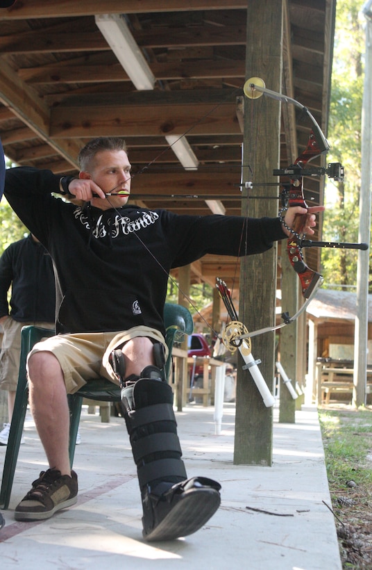 Cpl. Paul Kocina, attached to Wounded Warrior Battalion - West, prepares to let loose an arrow toward his target during the Archery Wounded Warrior Sports Camp at the archery range aboard Marine Corps Base Camp Lejeune, Oct. 6 through 10. Forced to sit due to his recovery from double compound fractures in both legs, Kocina, like many other wounded warriors attending the camp, find ways to work with their injuries when performing in various sport activities.