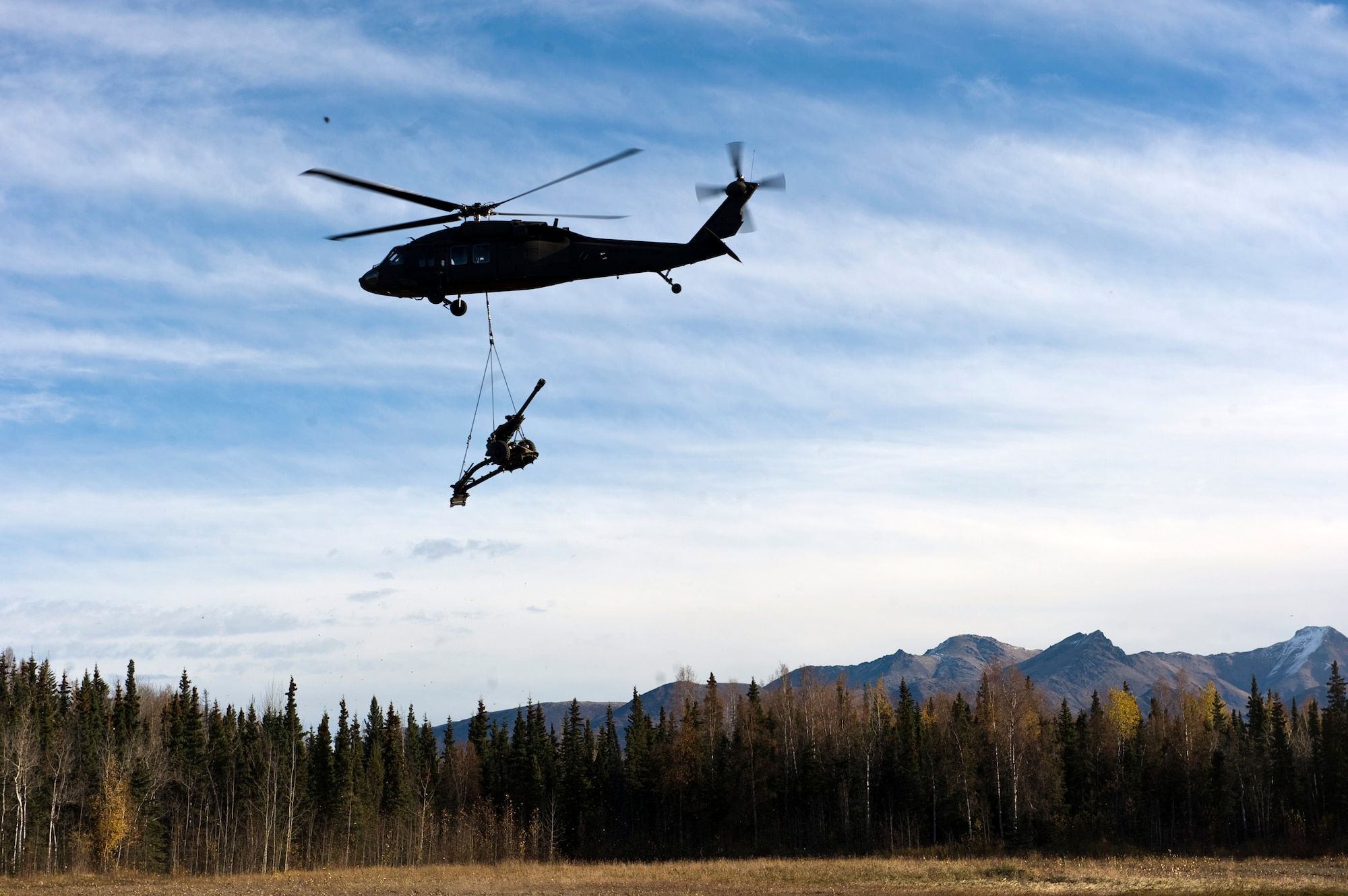 JOINT BASE ELMENDORF-RICHARDSON, Alaska -- An Army UH-60 Black Hawk flies with a 105 mm howitzer sling loaded to it Oct. 5. Soldiers from Alpha Battery from the 2nd Battalion of the 377th Parachute Field Artillery Regiment simulated a two-gun raid, firing into "enemy territory," as part of some mission-ready training. (U.S. Air Force photo/Airman 1st Class Christopher Gross)  