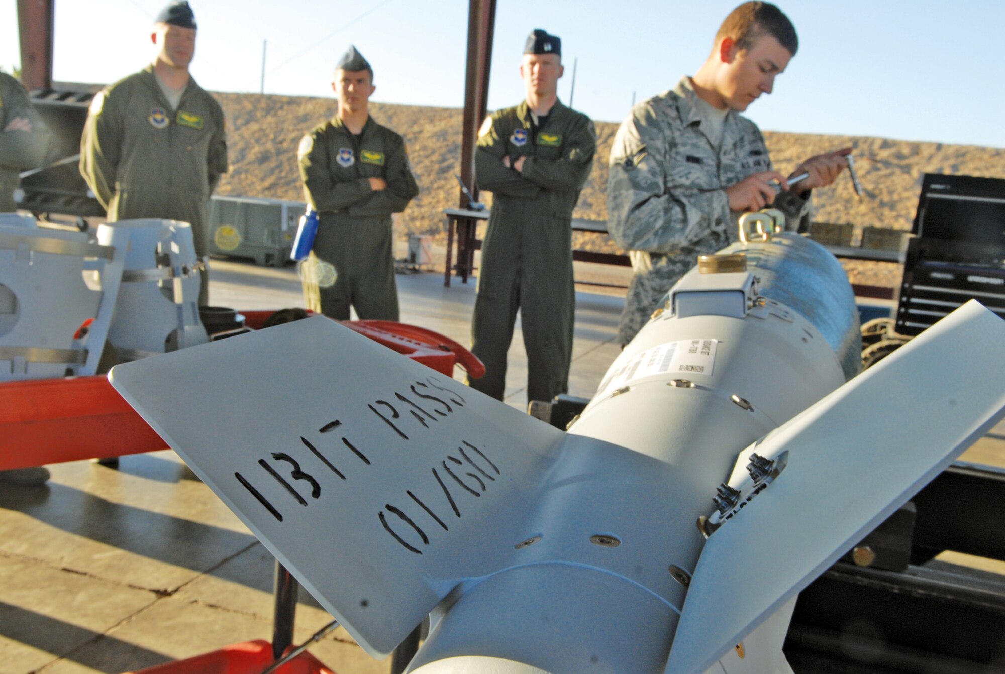 A bomb crew Airman works on the assembly of a GBU-38 inert bomb while a group of student pilots learns what it takes to assemble and deliver munitions to the flightline for training support.  (U.S. Air Force photo/Senior Master Sgt. Larry Schneck)
