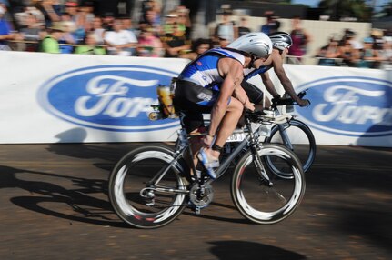 Maj. Scott Poteet adjusts his shoe as he speeds by the crowd after transitioning from the 2.4-mile swim to the 112-mile bike race while competing in the 2010 Ironman World Championship Oct. 9, 2010, at Kona, Hawaii.  Major Poteet is assigned to the U.S. Air Force Academy in Colorado Springs, Colo. He finished with an overall time of 9:39:05. (U.S. Air Force photo/Tech Sgt. Cohen A. Young)