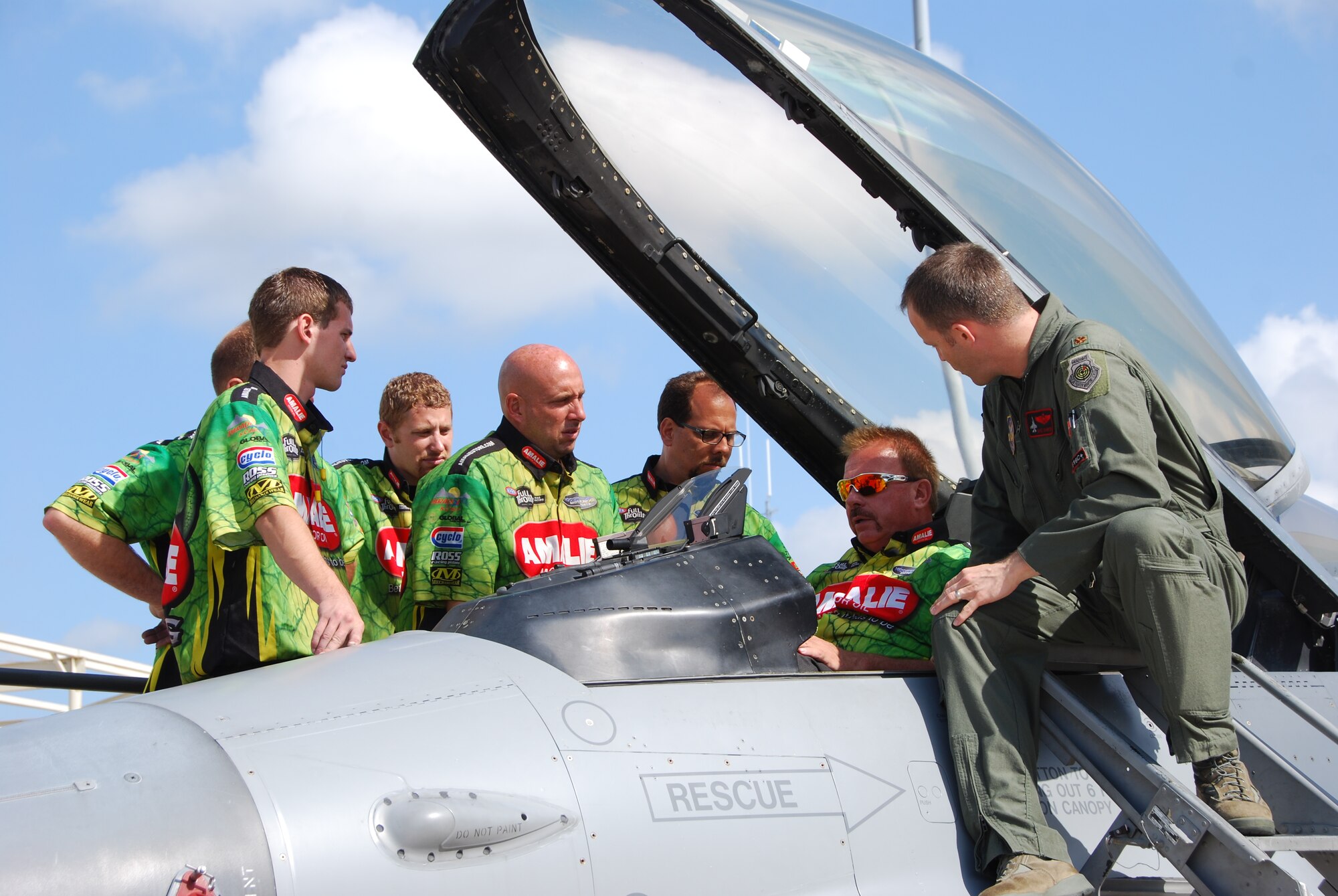 As Mr. Terry McMillen, driver of the Amalie Oil Top Fuel dragster, sits in the seat of the F-16, Maj. Michael Barron, right, pilot with the 457th Fighter Squadron, discusses the differences and similarities between the instrumentation of the jet and the racer. McMillen and his crew recently visited the 301st Fighter Wing before racing at a Dallas-area event. (Air Force Photo/Tech. Sgt. Shawn McCowan)