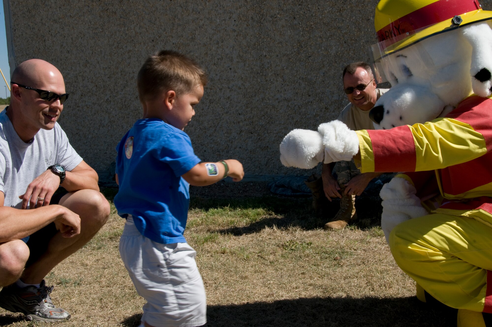 GOODFELLOW AIR FORCE BASE, Texas – Gunnar Truskett, 2, gives Sparky the Fire Dog a fist bump as 17th Contracting Squadron commander, Maj. Garrett Truskett looks on during the 6th annual Firefighter Muster at the fire station Oct. 8. The muster was part of the Fire Prevention Awareness Week, to spread the word on fire and smoke alarm safety. (U.S. Air Force photo/ Senior Airman Tong Duong)