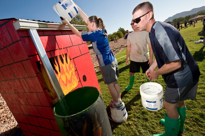 NELLIS AIR FORCE BASE, Nev.-- Master Sgt. Jennifer Buys (center) pours her bucket of water onto the roof of a house as Master Sgt. Lawrence Kirkley (foreground) waits his turn and Master Sgt. Robert Workman look on.  All three first sergeants participated in the bucket brigade event during the 4th annual Fire Muster competition at the Nellis Sport Pavilion Oct. 8.(U.S. Air Force photo by Lawrence Crespo) 
