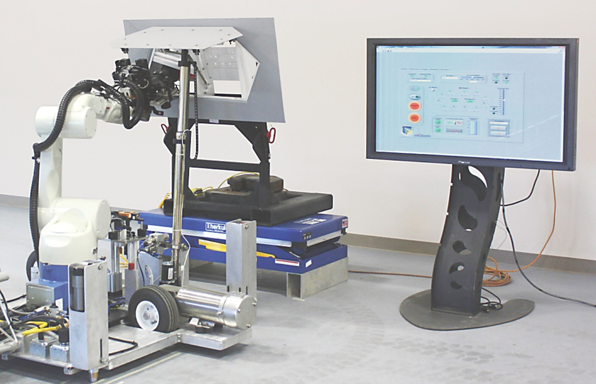 AFRL's Automated Aircraft Ground Refueling system prototype robot with fuel nozzle attached to a single-point refueling adapter inside the mock-up aircraft refueling panel.  The large screen displays the user interface. 
(Photo courtesy of A. Nichols,  AFRL/RXQ Robotics Group)