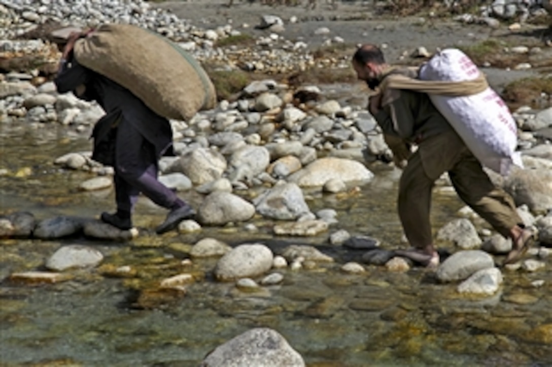 Two Pakistani men rush across a stream to load bags of food onto a U.S. Army CH-47 Chinook helicopter during relief operations in the Khoistan region, Pakistan, Oct. 12, 2010. The CH-47 crew is assigned to the 16th Combat Aviation Brigade, which is assisting victims of flooded areas.