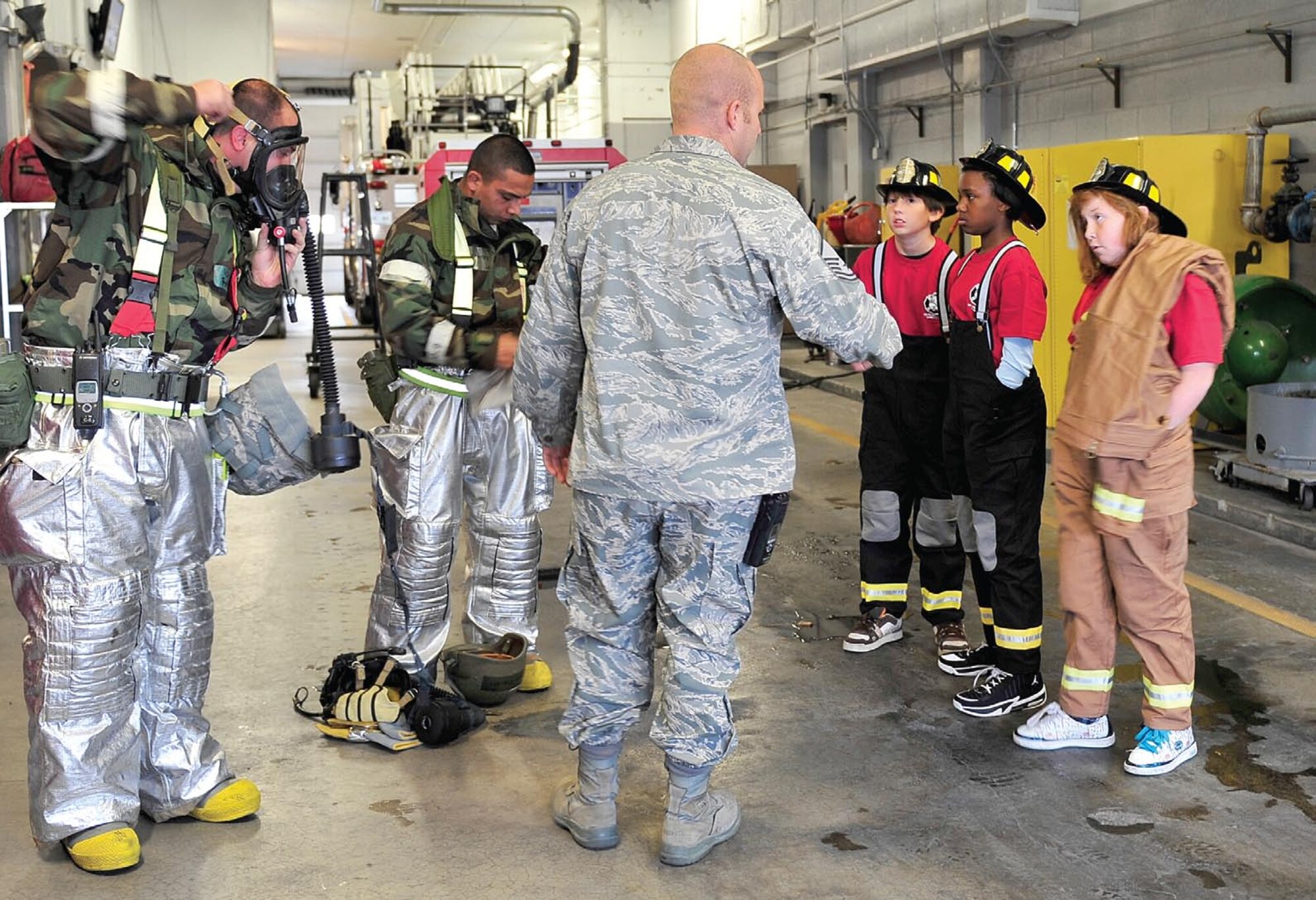 Tech. Sgt. Sam Roth, Staff Sgt. Derek Martinez and Master Sgt. Joshua Jex, all of the 419th Civil Engineer Squadron, explain to Kieran Murphy, Leah Young and Jasmin Fowler how their gas masks work for emergency calls. The Hill Field Elementary students were selected to be firefighters for a day after writing an essay on fire prevention. (U.S. Air Force photo/Kim Cook)