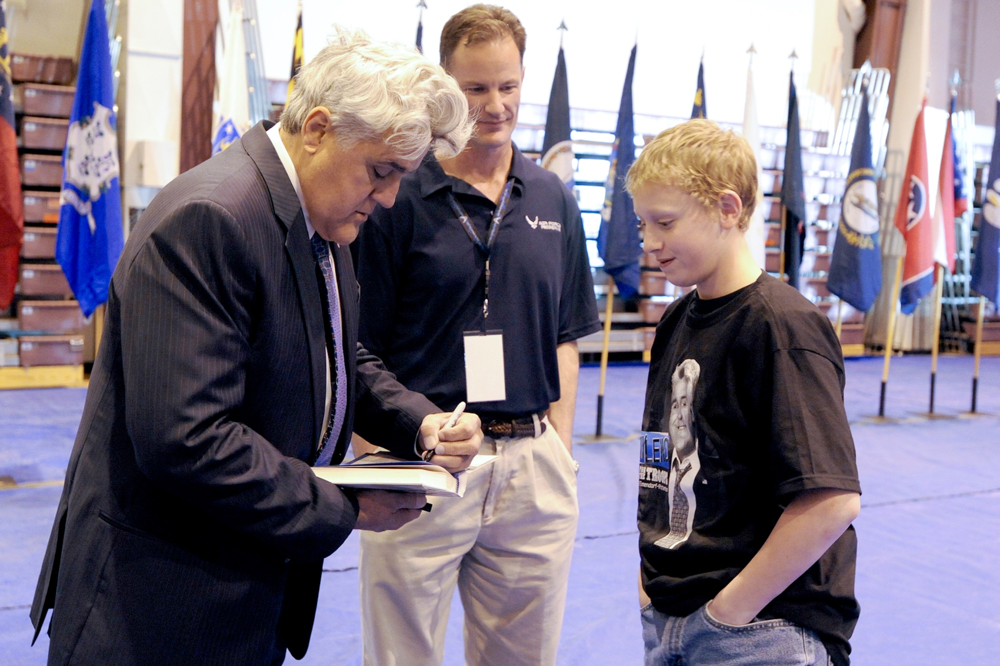 Jay Leno signs a copy of his autobiography for Jared Layton, the son of Senior Master Sgt. Timothy Layton, while Col. Eric Overturf looks on. Sergeant Layton is with the 962nd Aircraft Maintenance Unit. Colonel Overturf is the 477th Fighter Group commander. (U.S. Air Force photo\Staff Sgt. Joshua Garcia)