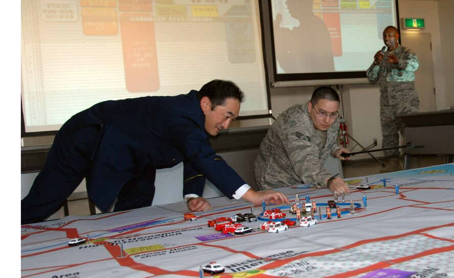 (Left to Right) Iwama Masatoshi, Misawa City Police subsection chief, and Senior Airman Robert Quinn, 35th Medical Group, demonstrate joint city and military response efforts during an emergency response table top exercise in Misawa City, Japan, Oct. 13, 2010. Chief Master Sgt. McHudson Theodore (far right), 35th Civil Engineer Squadron fire chief, explains base first response procedures to Misawa city and military officials. These exercises are vital to maintaining the strong bilateral relationship between the base and Northern Japan. (U.S. Air Force photo by 1st Lt. Cammie Quinn/Released)