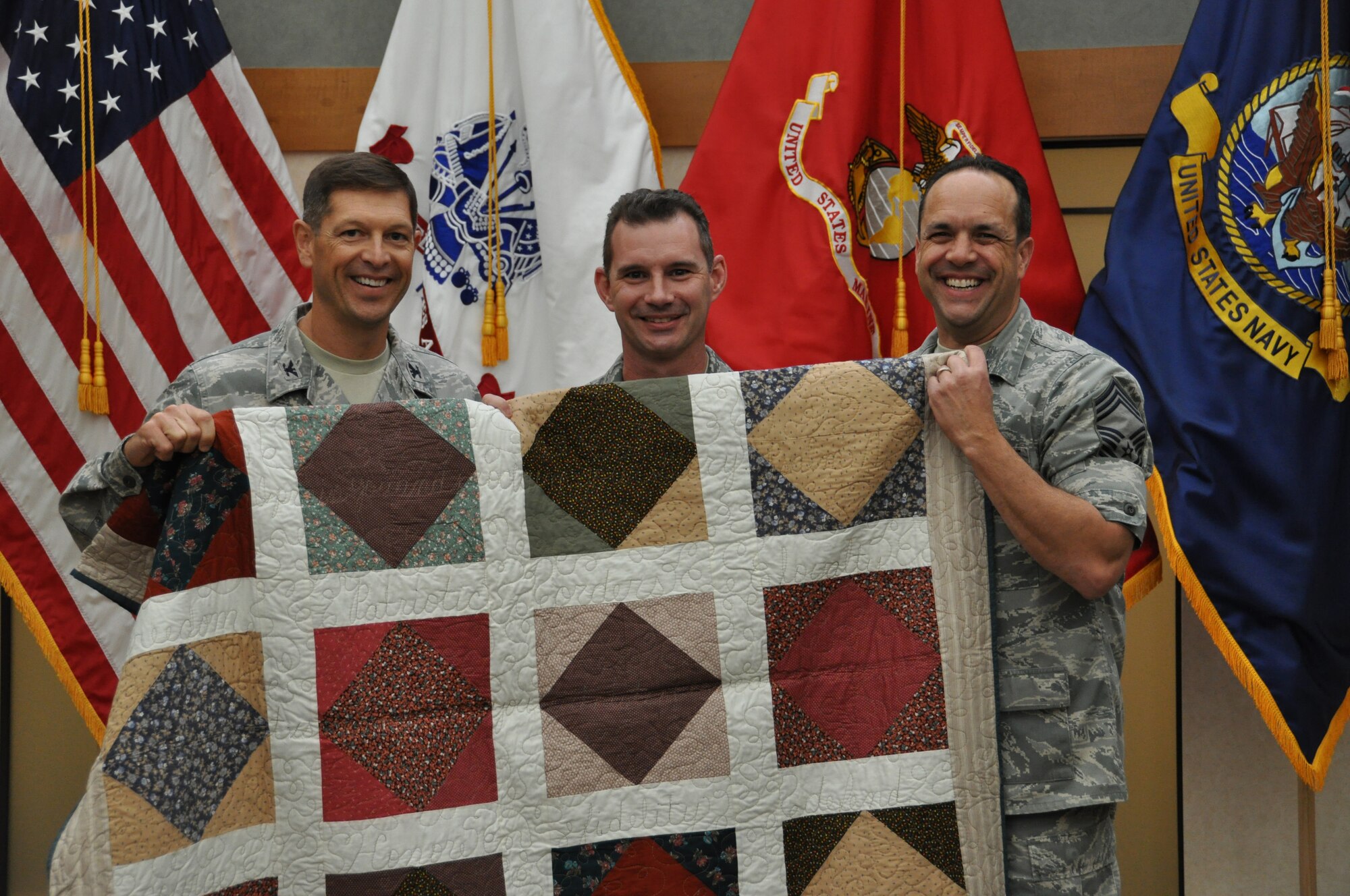 Col. Thomas C. Joyce, (left) Air Force Mortuary Affairs Operations Center commander, and Chief Master Sgt. David Fish, AFMAO chief enlisted manager, present a Quilt of Valor to Senior Master Sgt. Dan Walston, dignified transfer noncommissioned officer in charge, Oct. 14, for his support of fallen servicemembers. Volunteers from around the world make quilts for veterans and servicemembers touched by war. Sergeant Walston was deployed to AFAMO from Langley Air Force Base, Va., for a 179-day rotation. (U.S. Air Force photo/Staff Sgt. Christopher Bevins)
